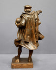 photo of bronze-colored plaster cast sculpture of standing man, namely Christopher Columbus, in robes and hat, pointing with right hand and holding a globe in his left arm against gray background