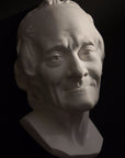 Photo with black background of plaster cast sculpture of elderly male head, namely Voltaire