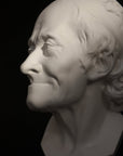 Photo with black background of plaster cast sculpture of elderly male head, namely Voltaire