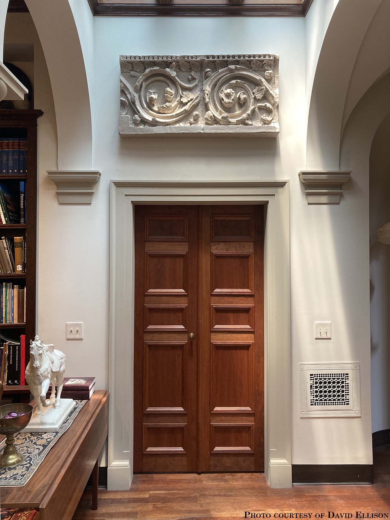 photo of plaster cast of architectural ornament with scroll and leaves above doorway in between archways in white-walled room