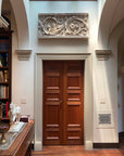 photo of plaster cast of architectural ornament with scroll and leaves above doorway in between archways in white-walled room