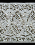 photo of white plaster cast of architectural ornament with geometric lines and leaf patterns in a row against black background