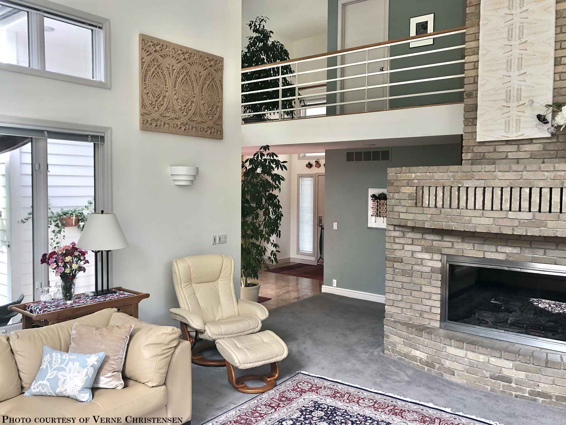 photo of plaster casts of an architectural ornament in terracotta color in a row on off-white wall in room with tan chairs and couch, rug, stone fireplace, and plants and green wall in background