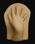 photo of off-white plaster cast sculpture of baby hand on panel against black background