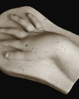 photo of off-white plaster cast sculpture of baby hand on panel against black background