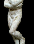 photo of antique plaster cast sculpture of nude female figure hugging herself against black background